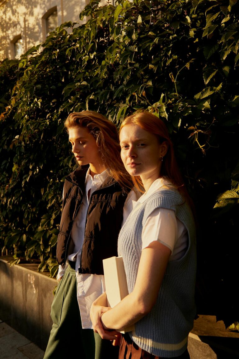 Two young students walk outside on a sunny day, surrounded by lush green foliage.